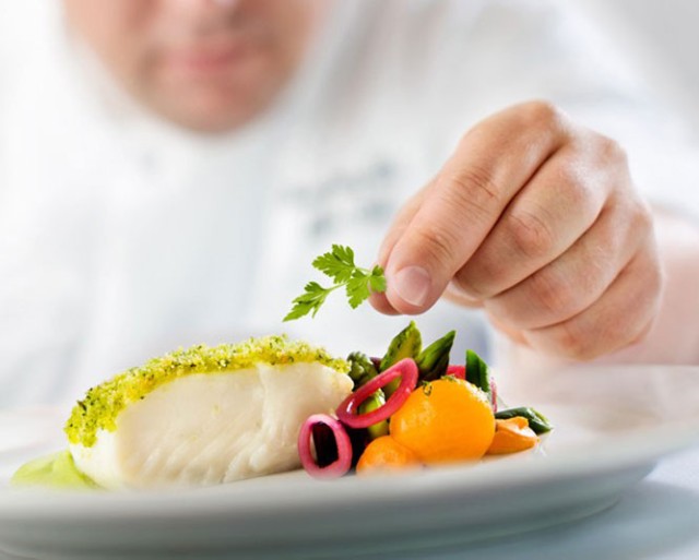 A closeup image of a chef adding to a dish.