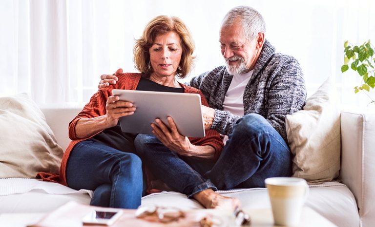 A couple sitting on the couch looking at their tablet.