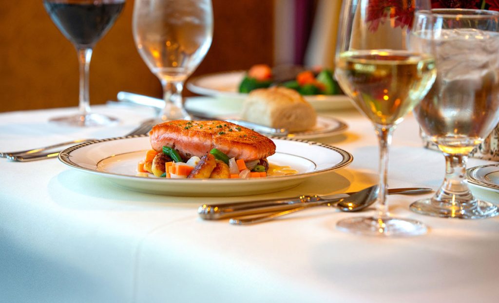 A fish dish on a fancy table with various wines.
