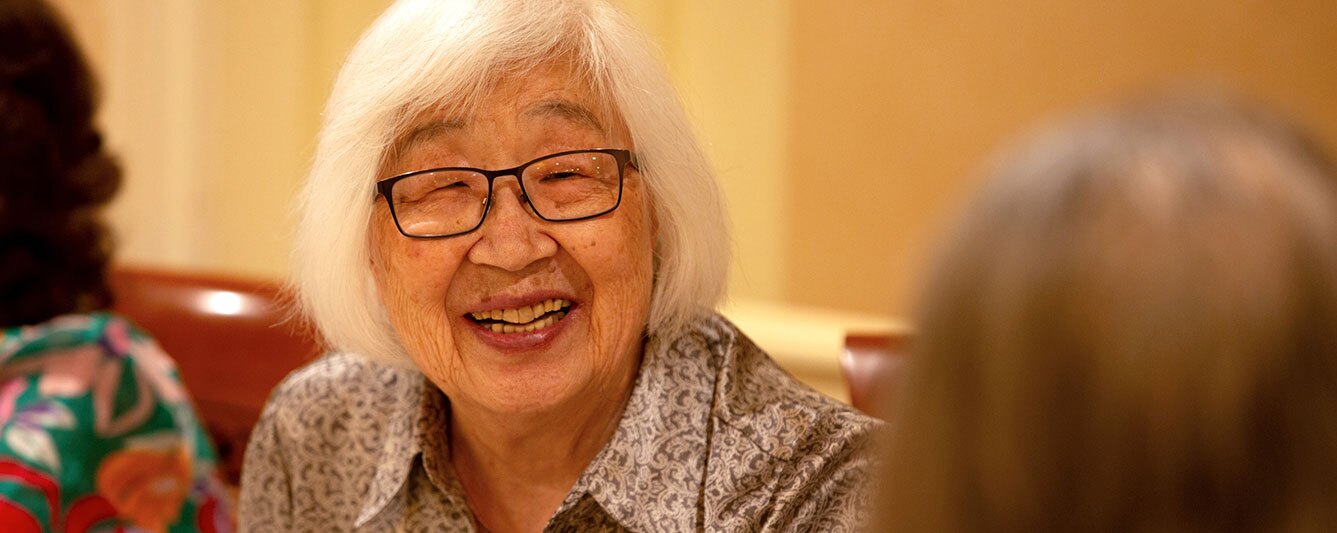 A woman smiling to another in the foreground.