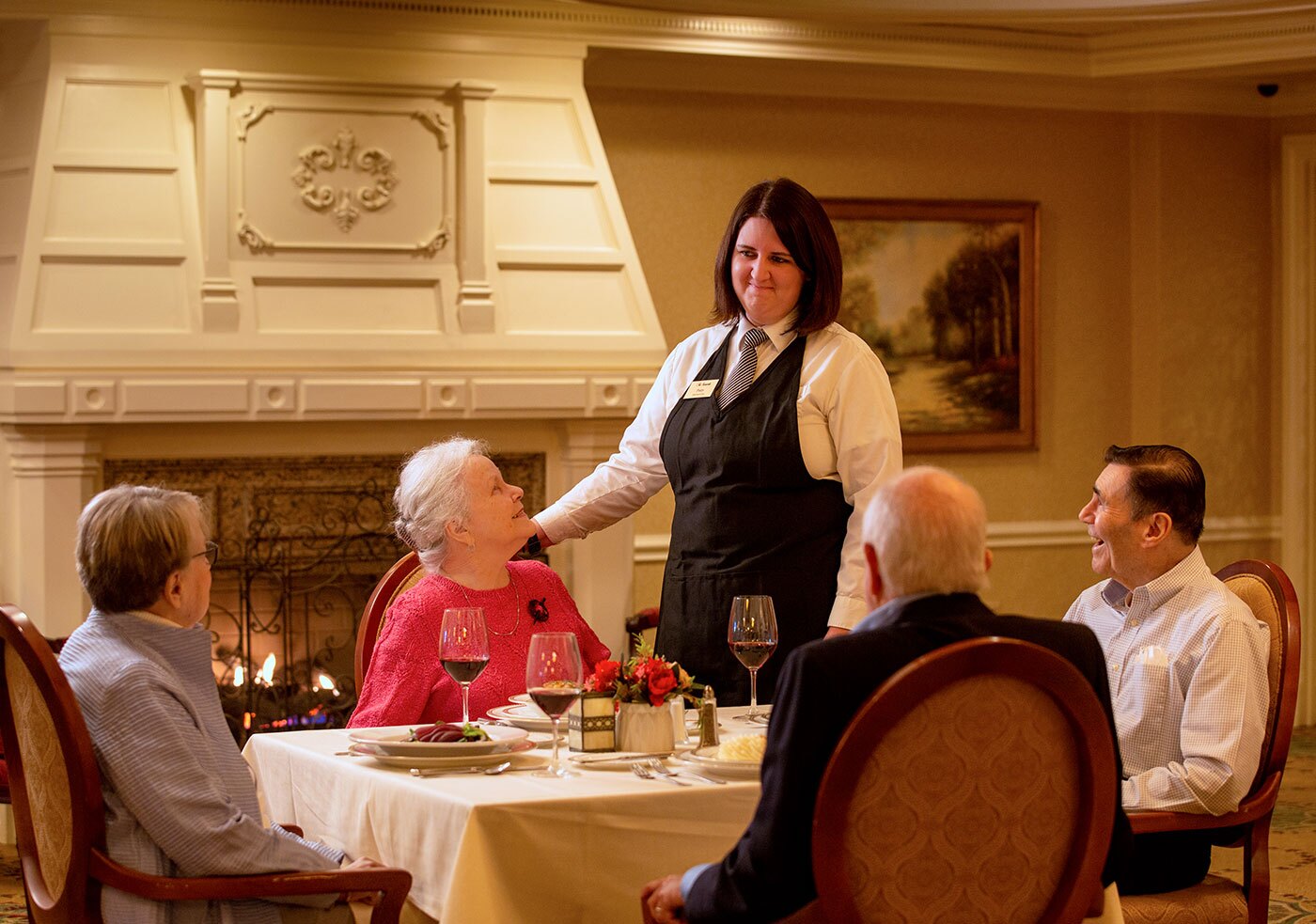 Team member standing and talking with four resident diners in the dining room.