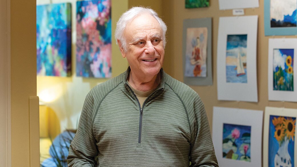 A man stands in front of his hanging artwork.