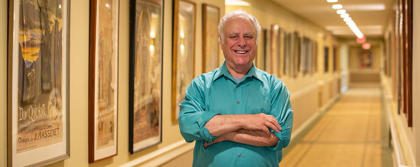 A man stands in the hallway with his artwork hanging.