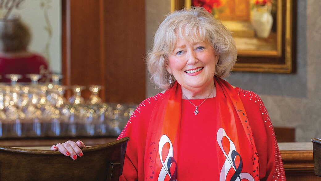A woman stands next to a barstool smiling.