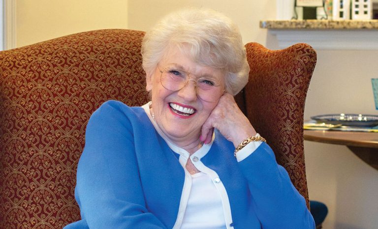 Resident sitting in a chair with her face leaning on her hand smiling.