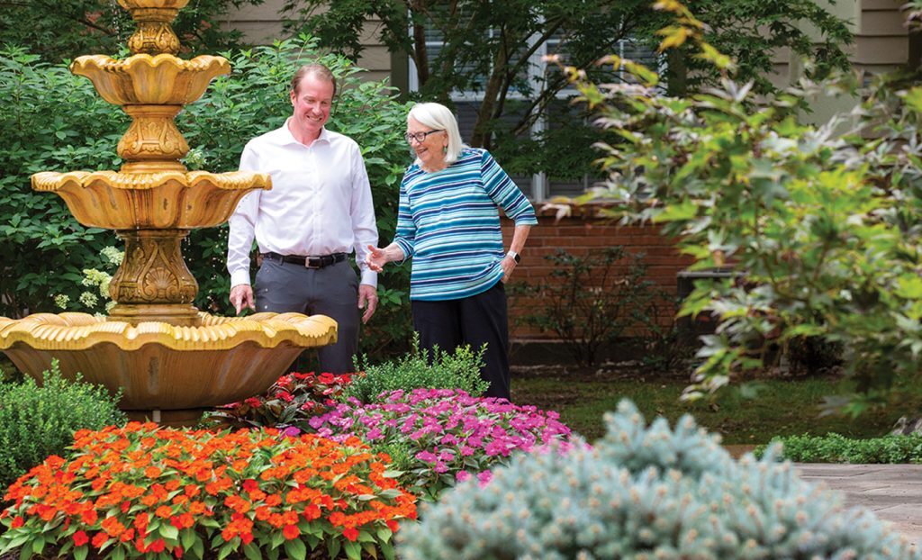 Chris Leonard and resident outside in garden with fountain.