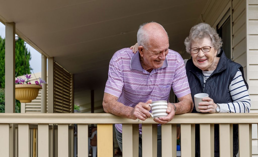 A husband and wife enjoying warm drinks on the porch.