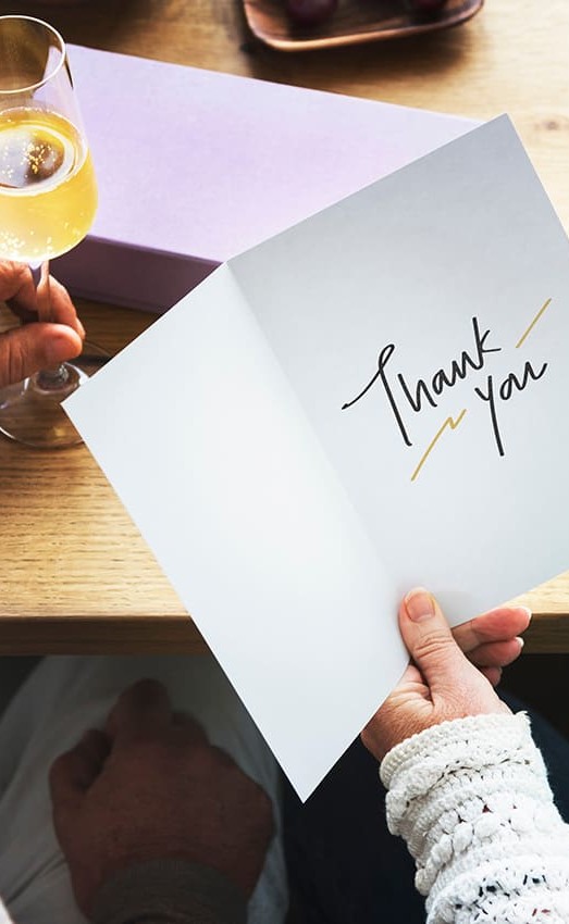 Senior couple enjoying wine - woman has greeting card with sentiment "Thank You"