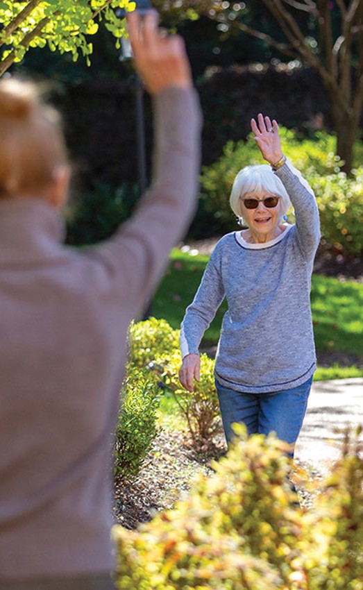 Two residents waving to each other outdoors.