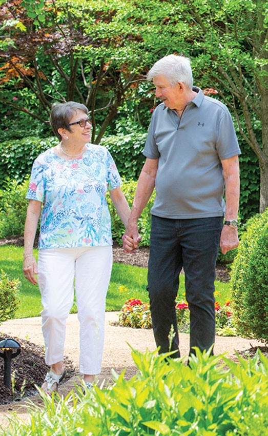 A couple walks down an outside path surrounded by nature while holding hands.