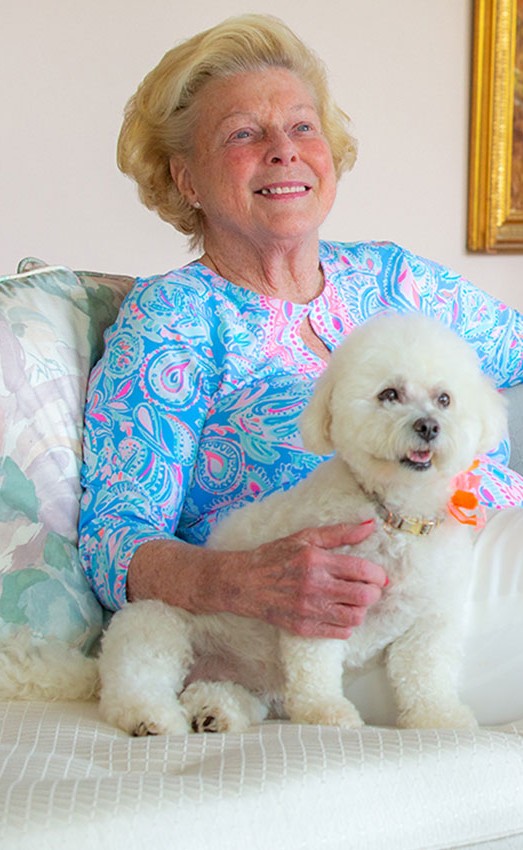 A resident sitting on a sofa holding her white dog.