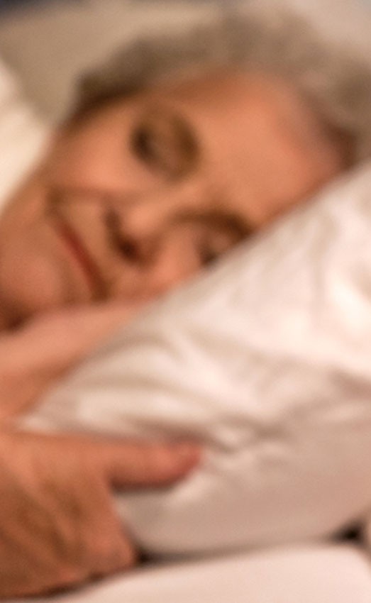 An alarm clock on a nightstand with a woman slipping in the background.