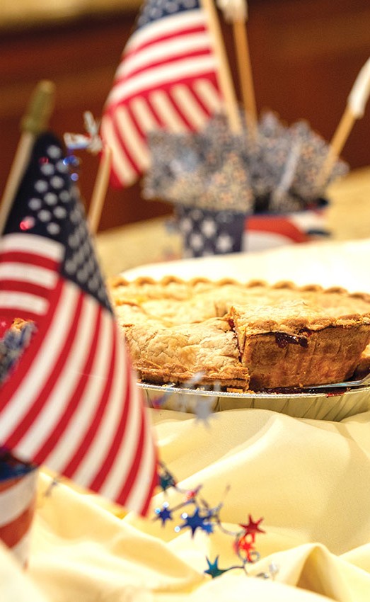 Cherry pie sitting on a dessert table with American flags.
