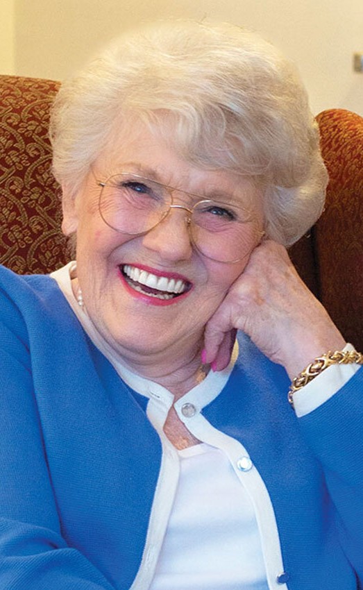 Resident sitting in a chair with her face leaning on her hand smiling.