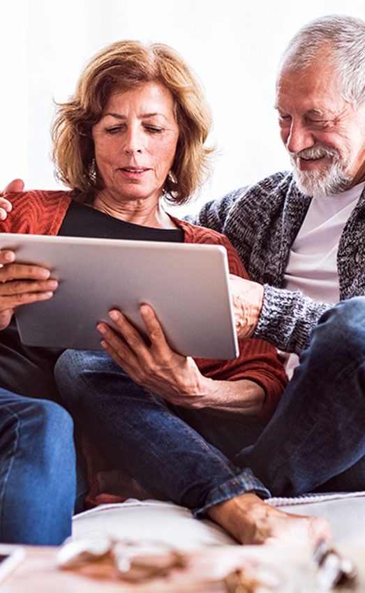 A couple sitting on the couch looking at their tablet.