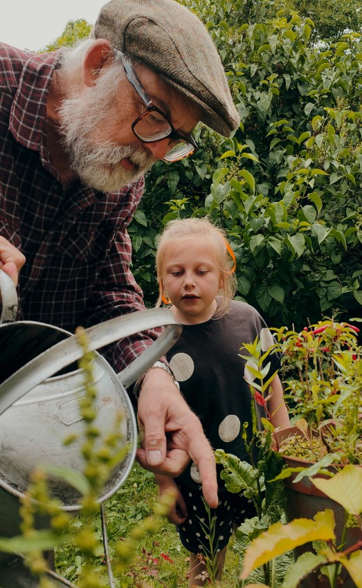A man waters plants with his grandchild, demonstrating a healthy intergenerational relationship.
