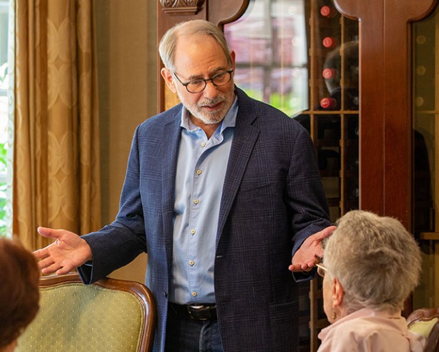 A man standing speaks with a few residents sitting down.