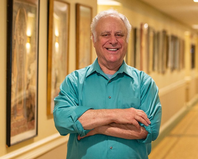 A man stands in the hallway with his artwork hanging behind him.