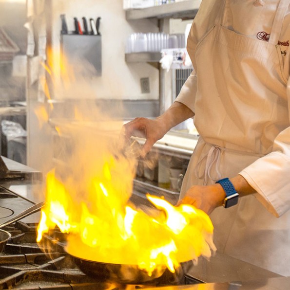 A chef cooking in the kitchen with and pan and fire.
