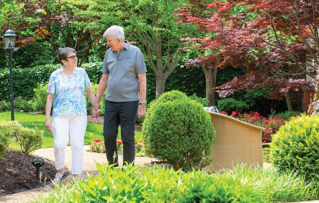 A couple walks down an outside path surrounded by nature while holding hands.