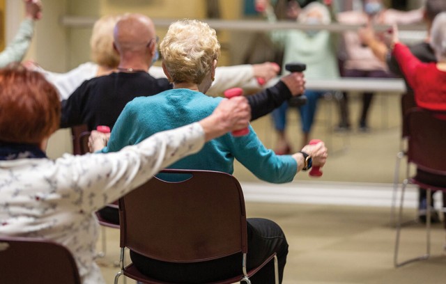 Residents in an exercise class sitting in chair lifting waits facing a mirror.