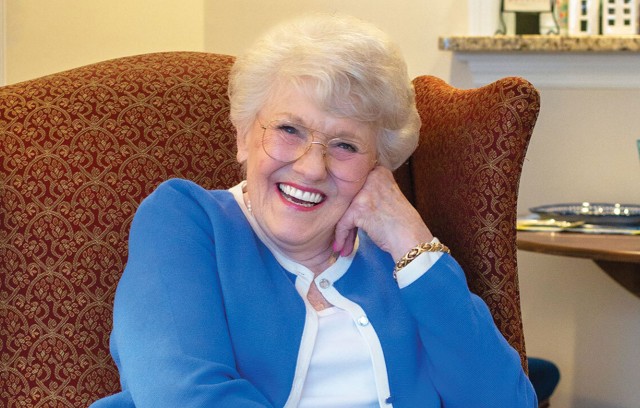 Resident sitting in a chair with her face leaning on her hand smiling.