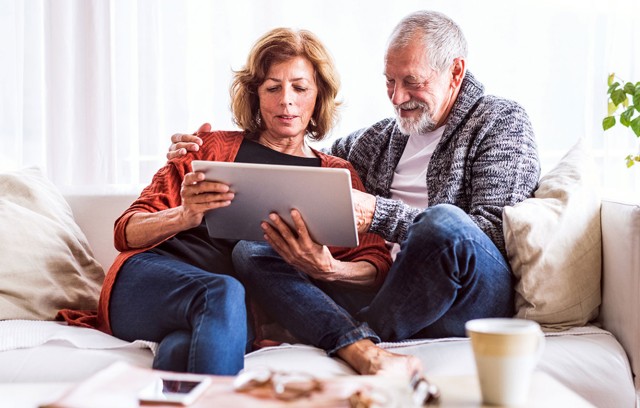 A couple sitting on the couch looking at their tablet.