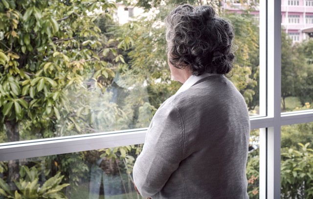 A woman looks out her window on an overcast day thinking.