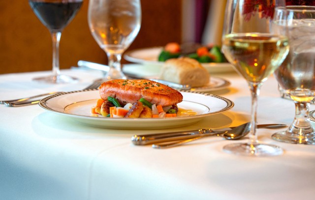 A fish dish on a fancy table with various wines.
