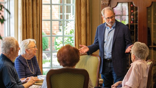 A man standing speaks with a few residents sitting down.