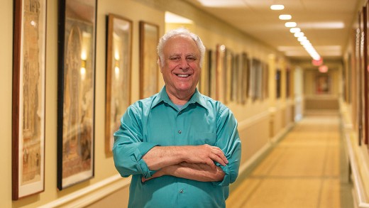 A man stands in the hallway with his artwork hanging.