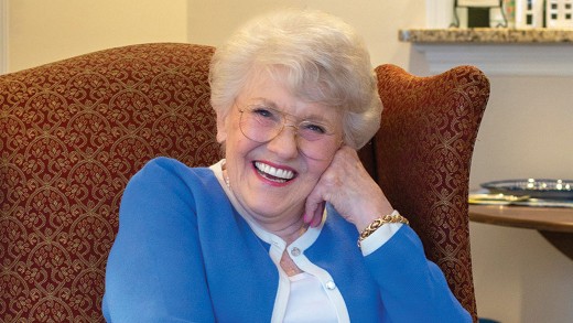 A resident sitting and smiling at the camera with her hand on her cheek.