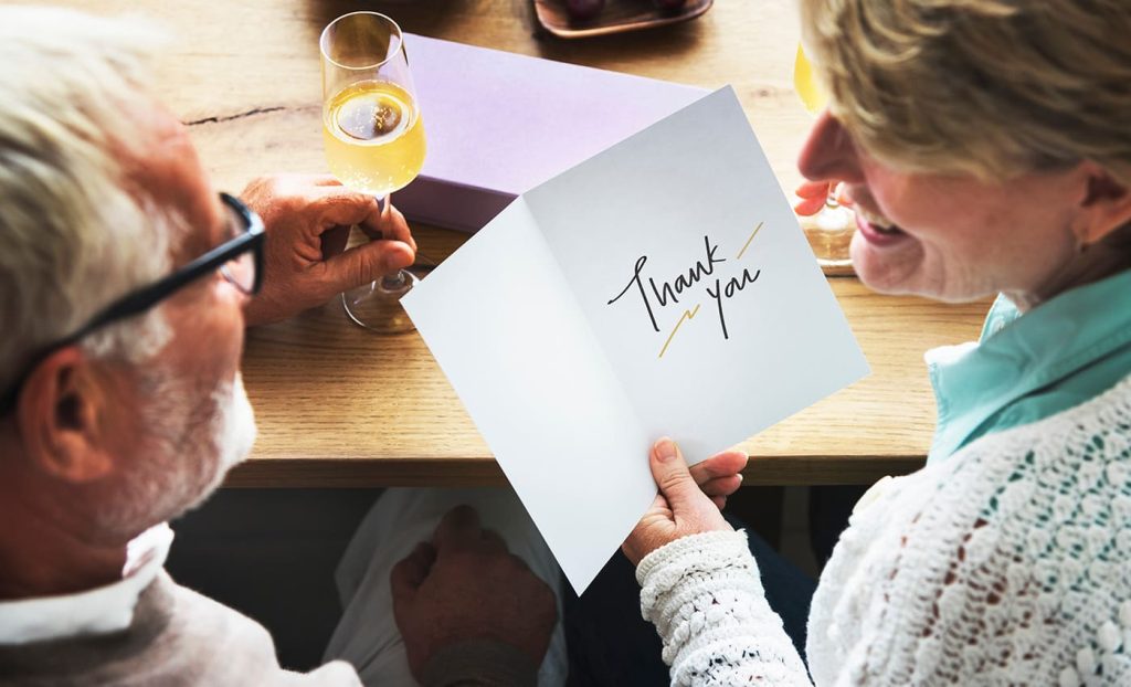 Senior couple enjoying glasses of whine - woman holds greeting card with sentiment "Thank You"