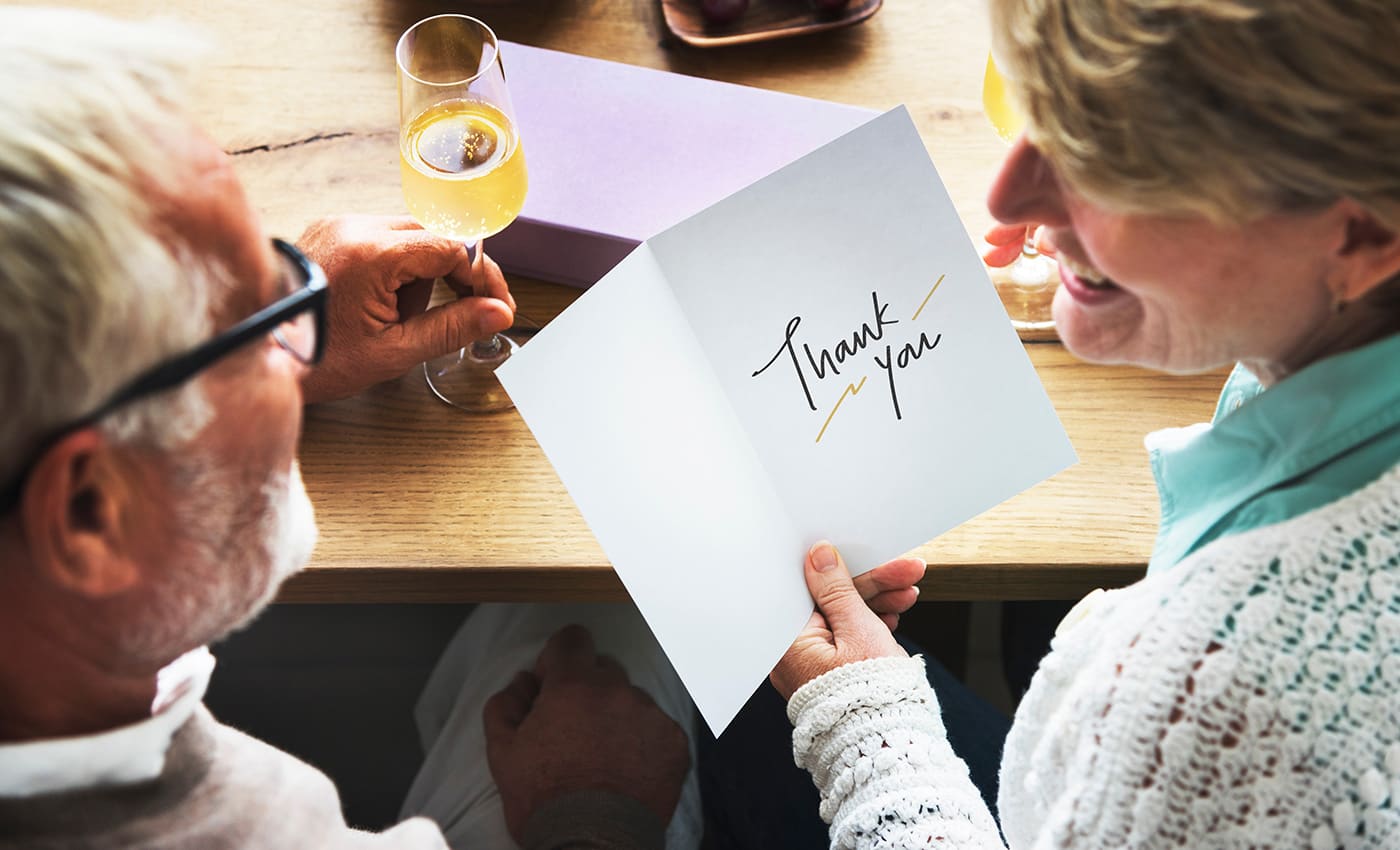 Senior couple enjoying glasses of whine - woman holds greeting card with sentiment "Thank You"