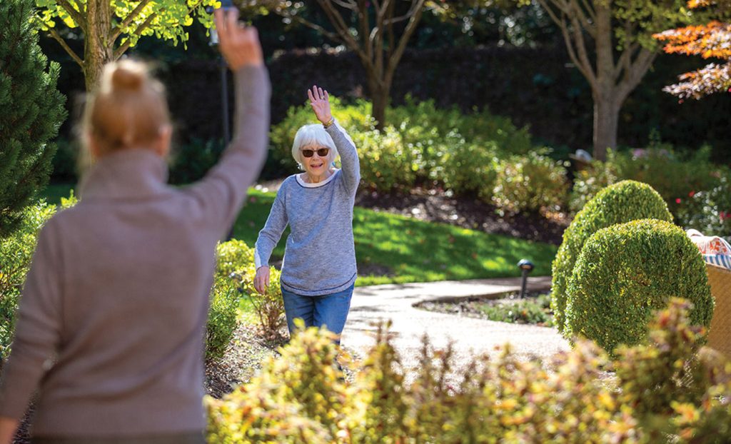 Two residents waving to each other outdoors.