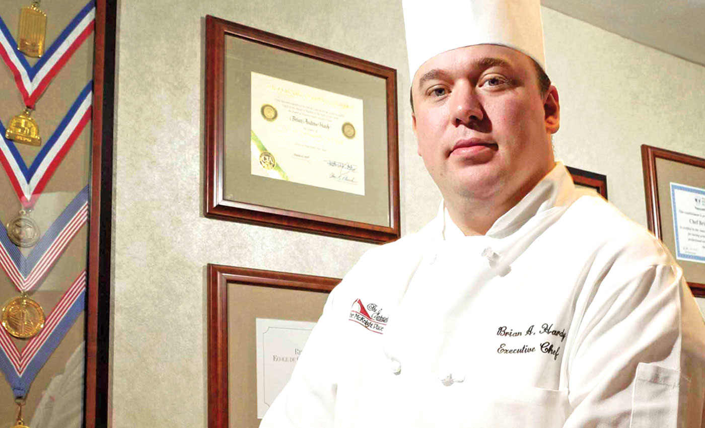 Executive Chef Brian Hardy in front of medals and certificates.