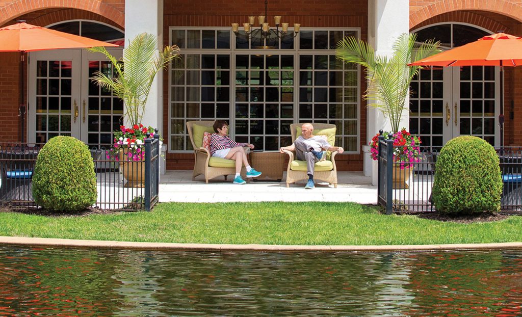 Two residents sitting and talking on the patio across the pond.