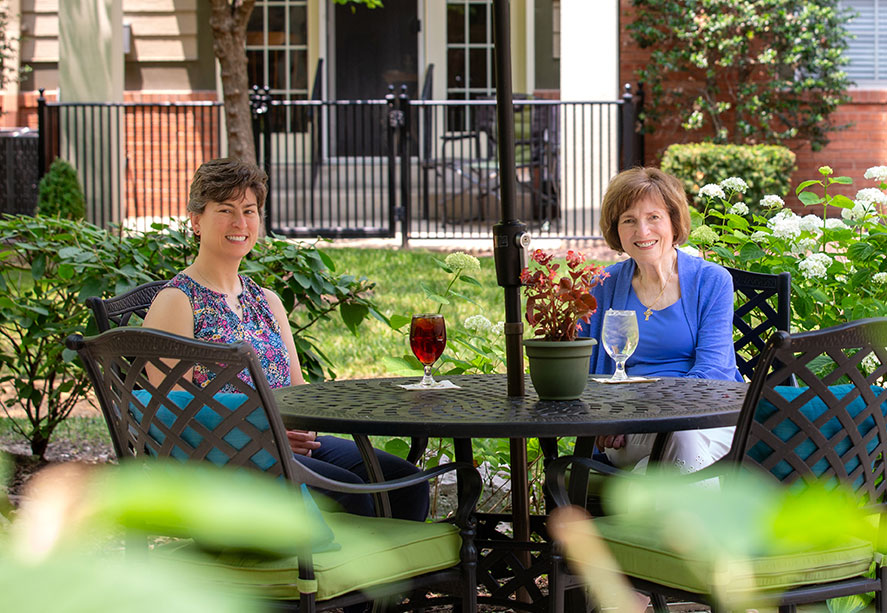 Two women sitting outdoors at patio table enjoying drinks.